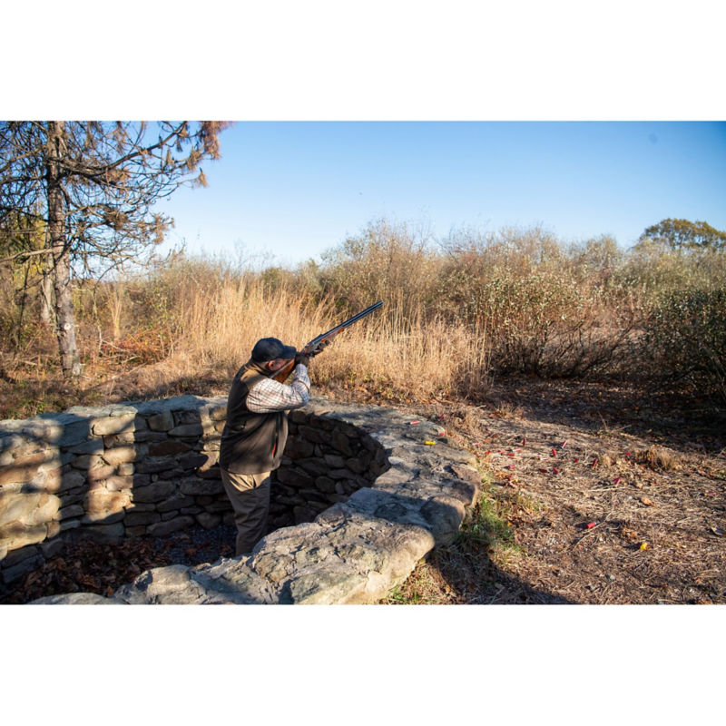A man standing behind a stone wall practicing his shot.